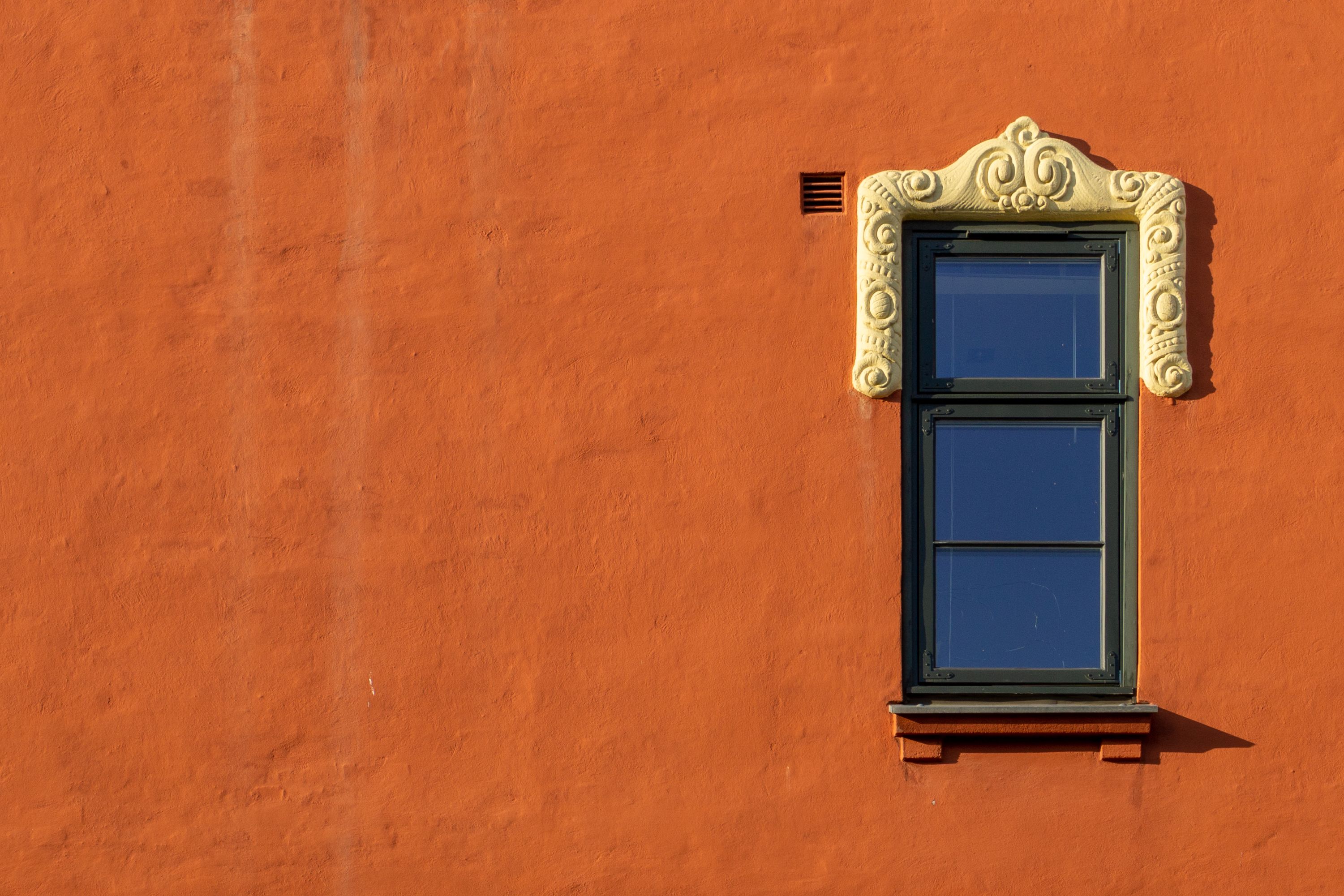 A detailed view of an ornate window set in an orange stucco wall, showcasing rustic architecture.