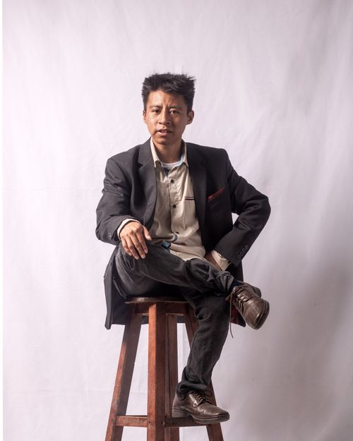 Free Portrait of a young man in smart casual attire sitting on a stool indoors. Stock Photo