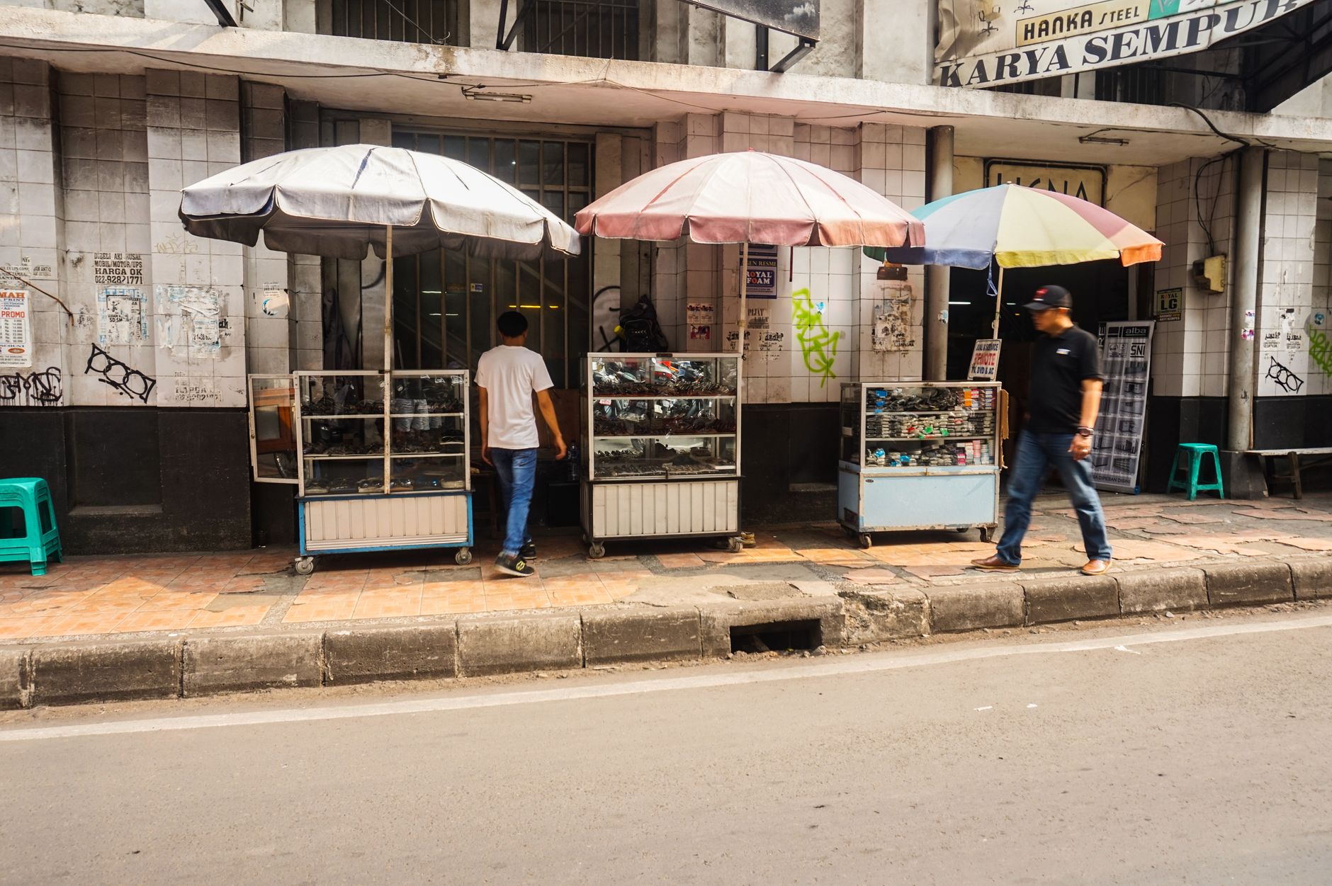 Outdoor street vendor stalls with umbrellas and walking pedestrians in a city setting.