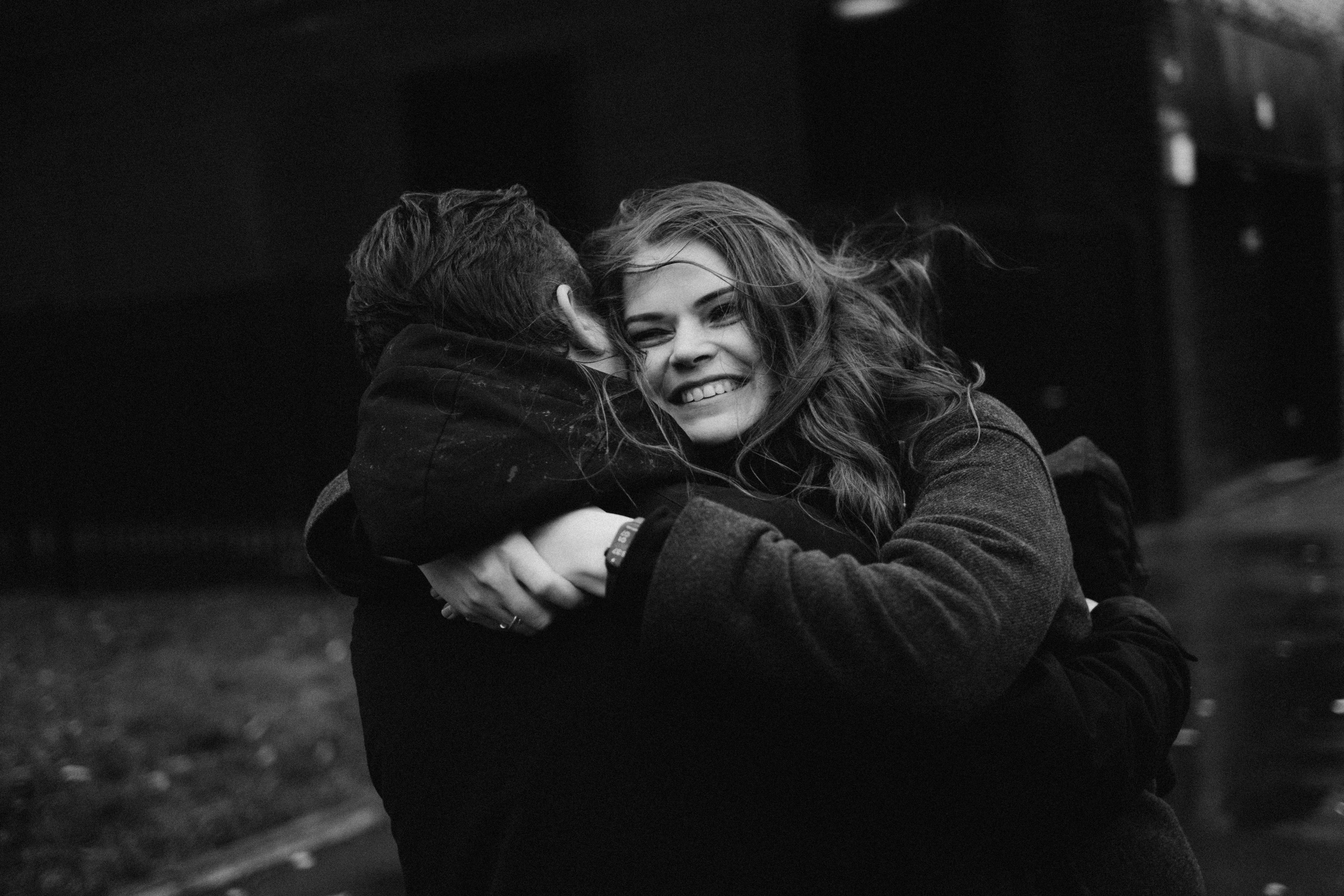 A joyful couple embraces on a dimly lit street, capturing warmth in a black and white setting.