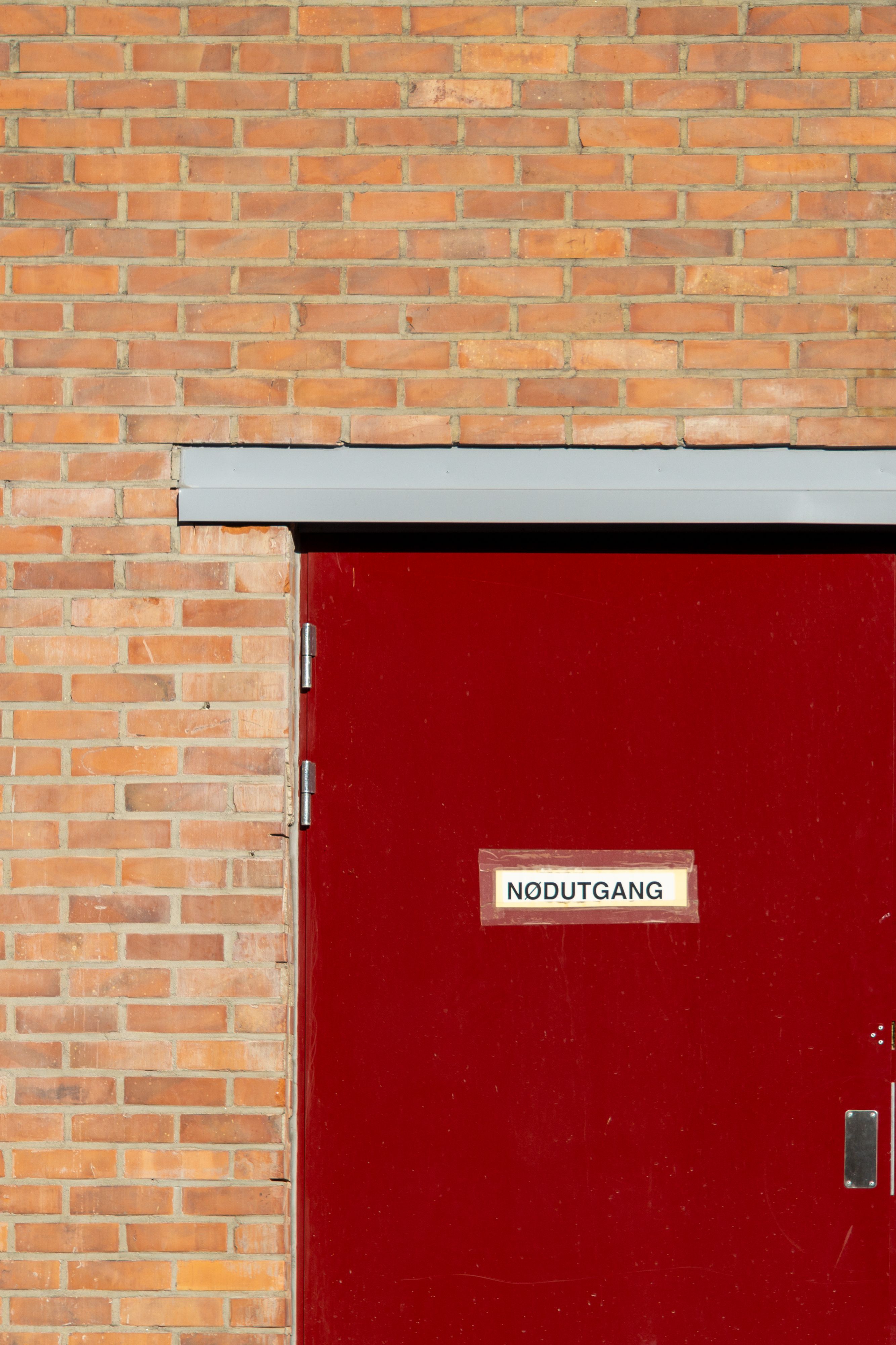 Close-up of a red emergency exit door against a brick wall, vibrant urban exterior in Oslo.