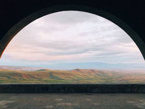 View through Charents Arch in Armenia with rolling hills and cloudy sky, perfect for travel inspo.