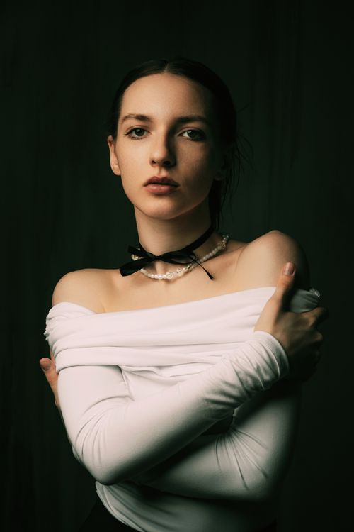 Free A fashion portrait of a woman with arms crossed, wearing a white blouse and necklace. Stock Photo