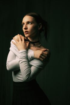 Charming studio portrait of an elegant woman in a white blouse with a contemplative pose against a dark background.