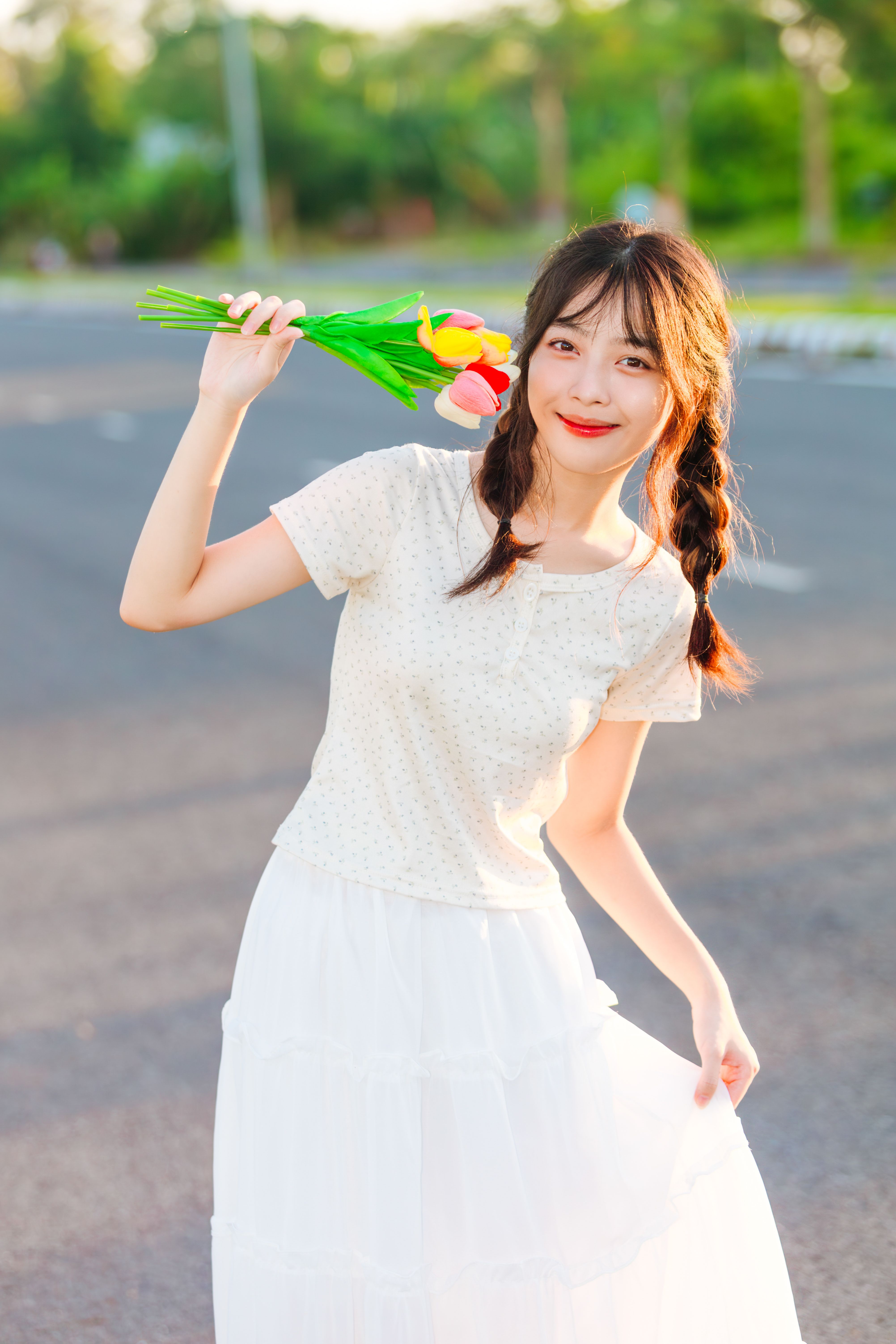 A Young Girl in a White Dress Standing Outside and Holding Flowers ...