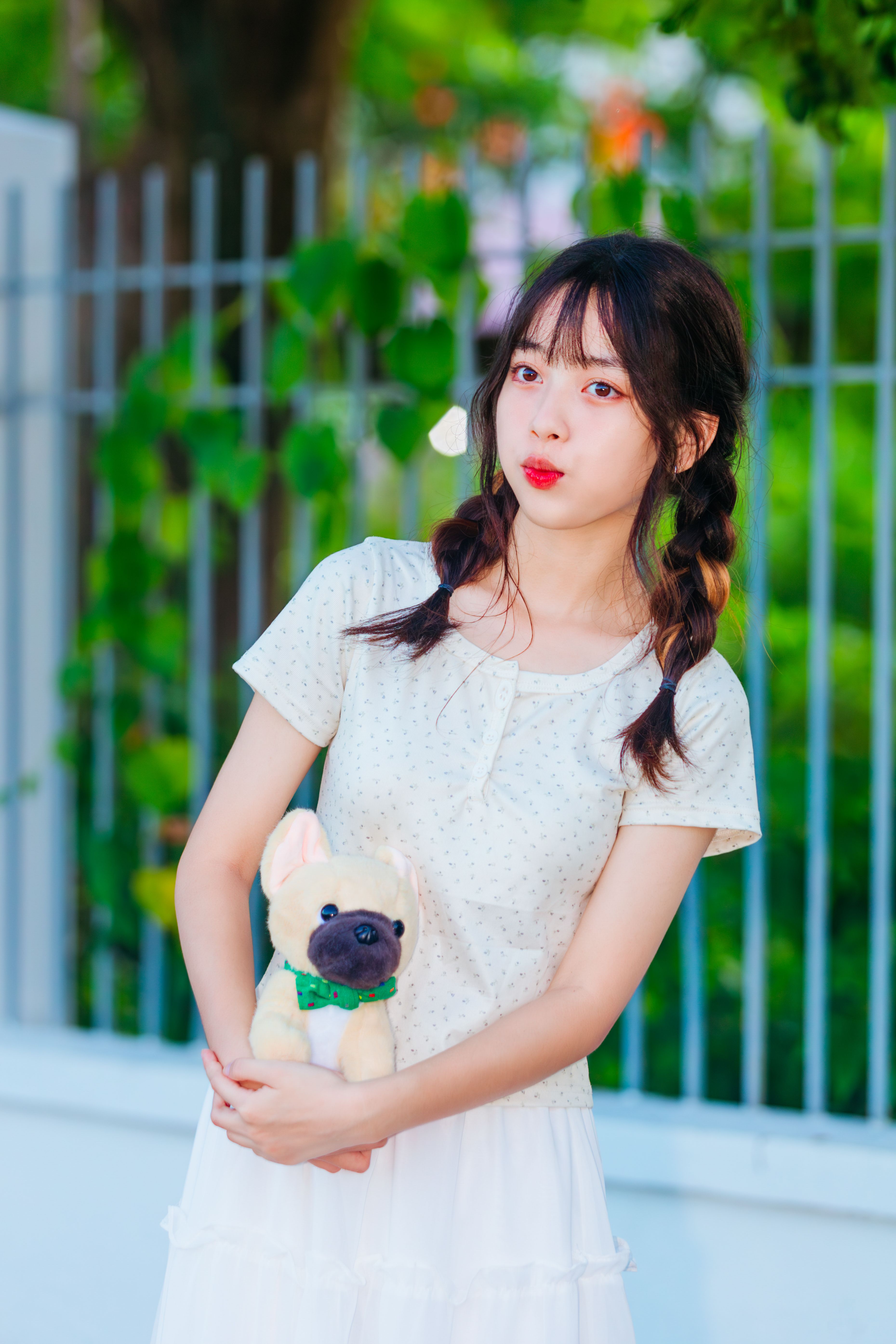 Young woman with braided hair holding a toy dog, standing outdoors against a fence.