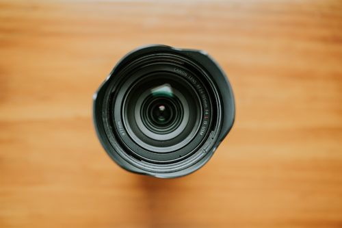 Free A detailed top view of a camera lens showcasing its intricate design on a wooden background. Stock Photo