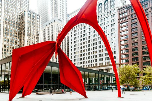 Vibrant red sculpture in a bustling Chicago plaza with towering skyscrapers.