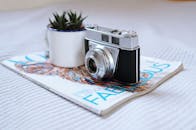 一台老式相机放在杂志上，旁边有一个杯子和一棵小植物