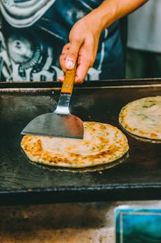 A close-up of a paratha being prepared on a hot griddle by a vendor. Perfect for food blogs.