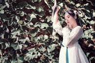 Woman Holding Hand fan Standing Beside Green Leafed Plant