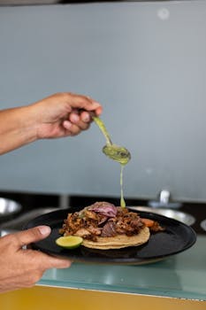 Close-up of a hand pouring sauce over a taco served on a black plate at a restaurant in Santiago de Querétaro, Mexico.