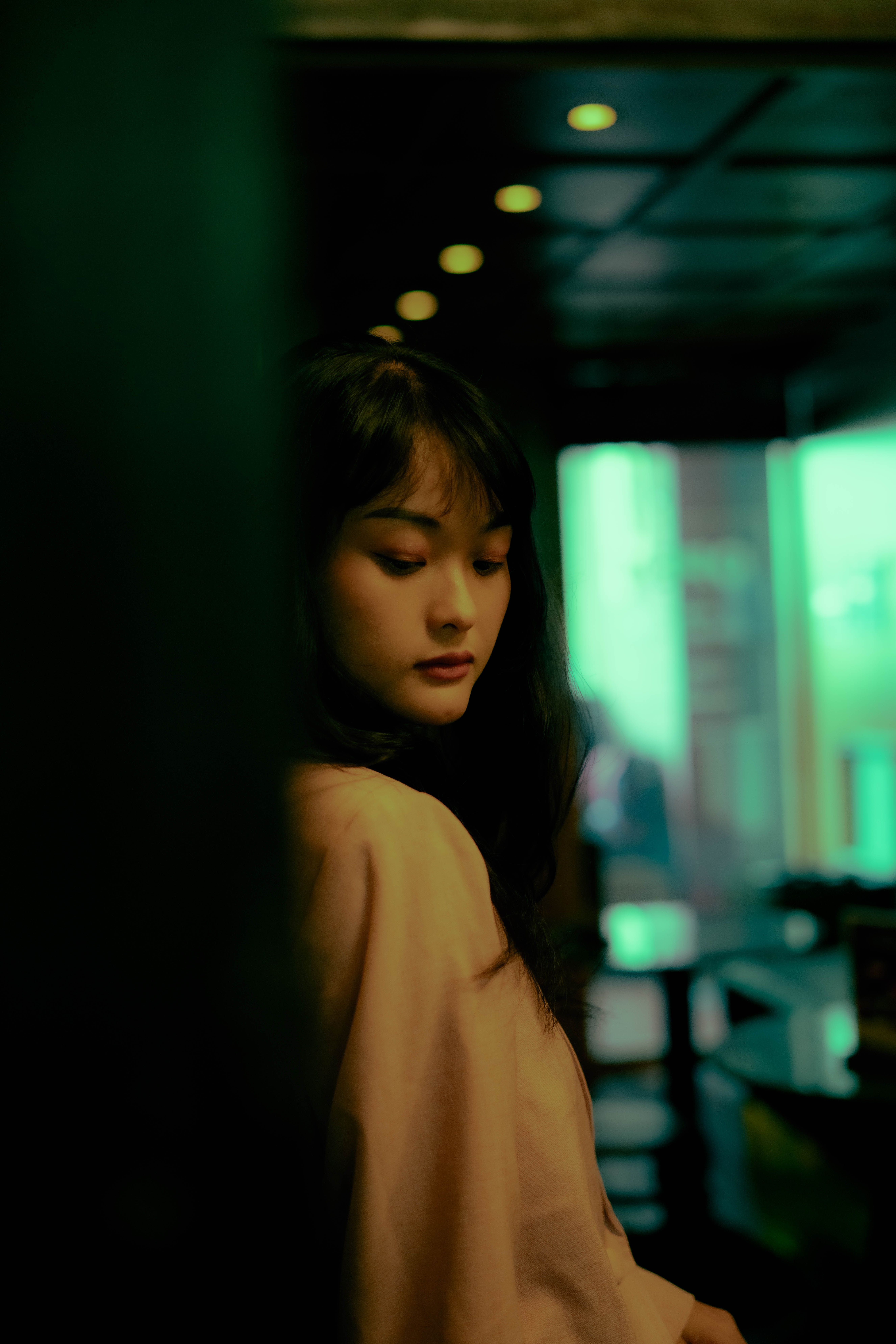 A contemplative portrait of a woman with ambient green lighting in an indoor setting.