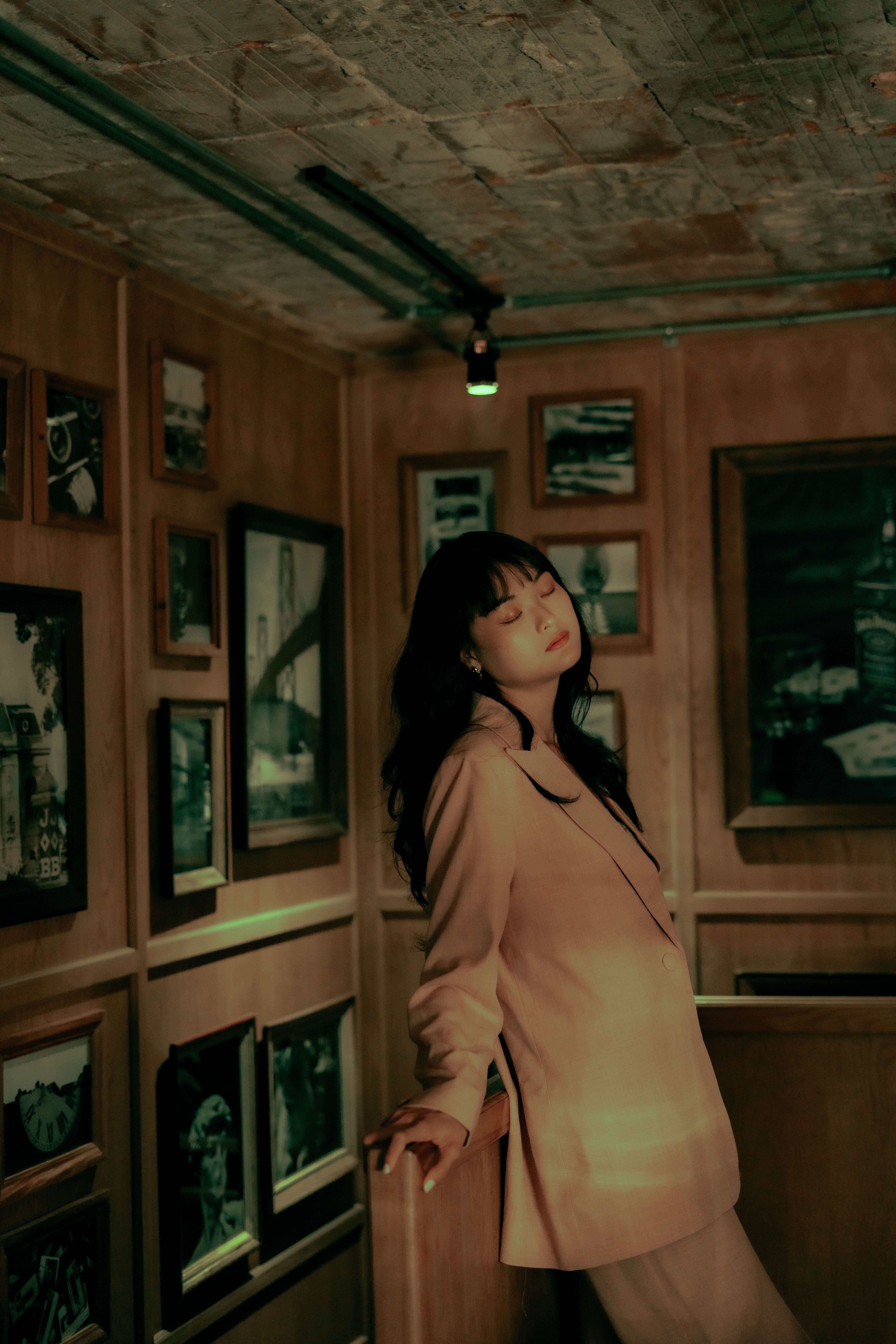 Elegant portrait of a woman in a pink jacket posing gracefully in a cozy gallery room.