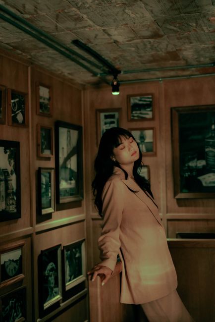 Elegant portrait of a woman in a pink jacket posing gracefully in a cozy gallery room.