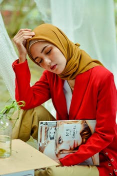 一位头戴头巾、身穿红色西装外套的年轻女子在室内拿着一本杂志