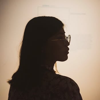 一个戴着眼镜的女人，在明亮的背景下摆出体贴姿势的剪影