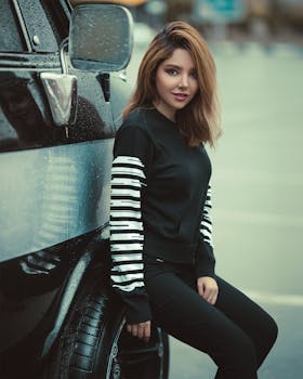 在潮湿的城市环境中，一位穿着休闲服的时尚女性在车辆旁摆姿势