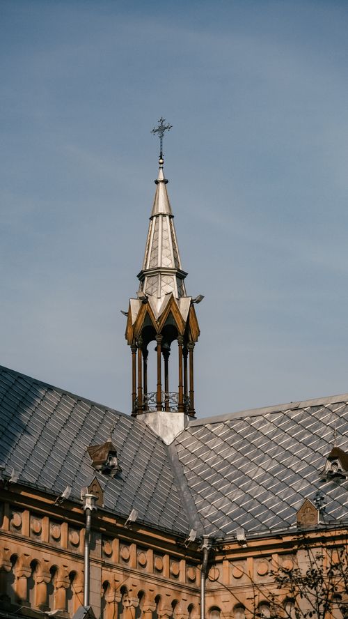 Free A majestic church spire rising above a historic European building under a clear blue sky. Stock Photo