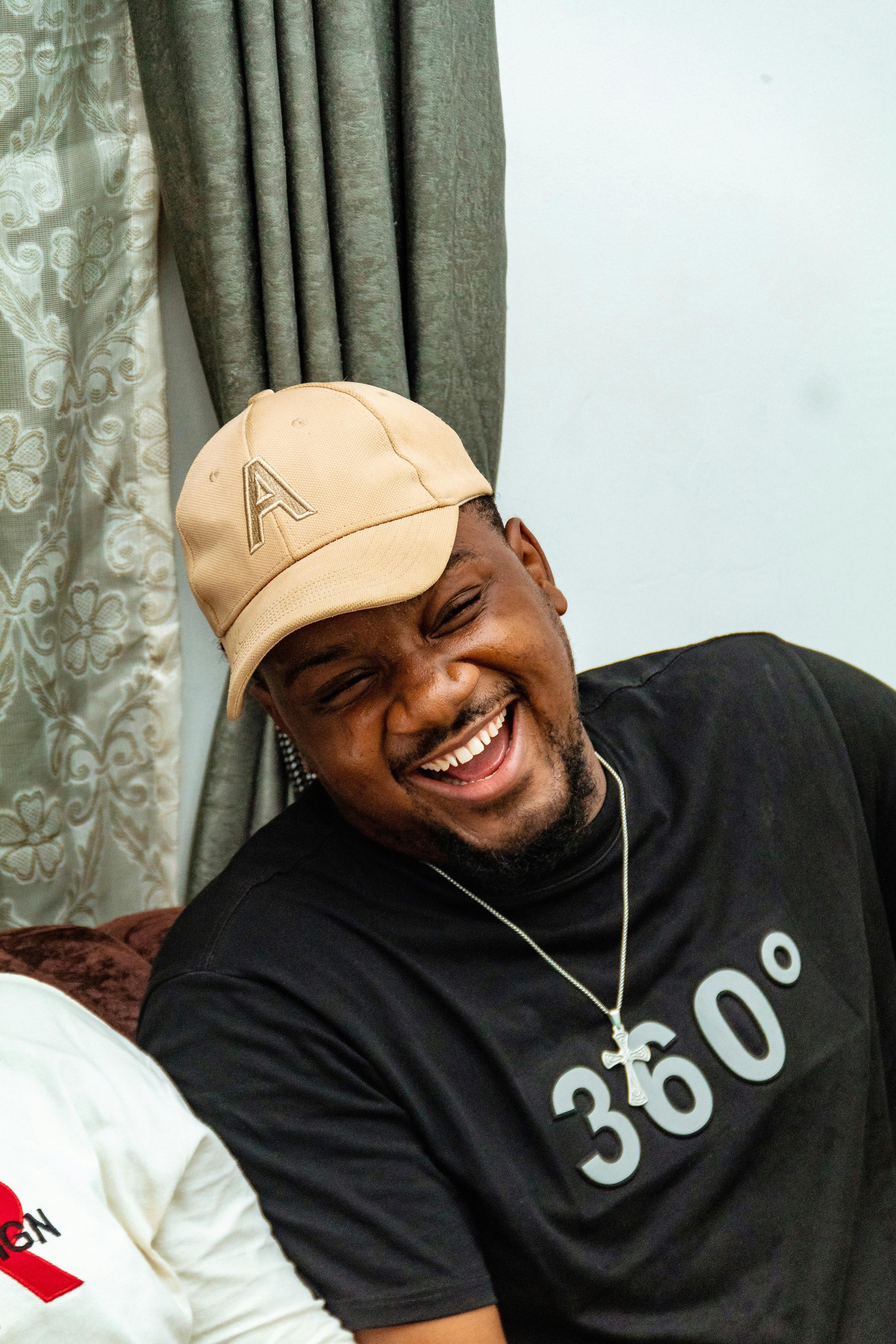 Smiling man in a beige cap and 360° t-shirt enjoys a moment indoors.