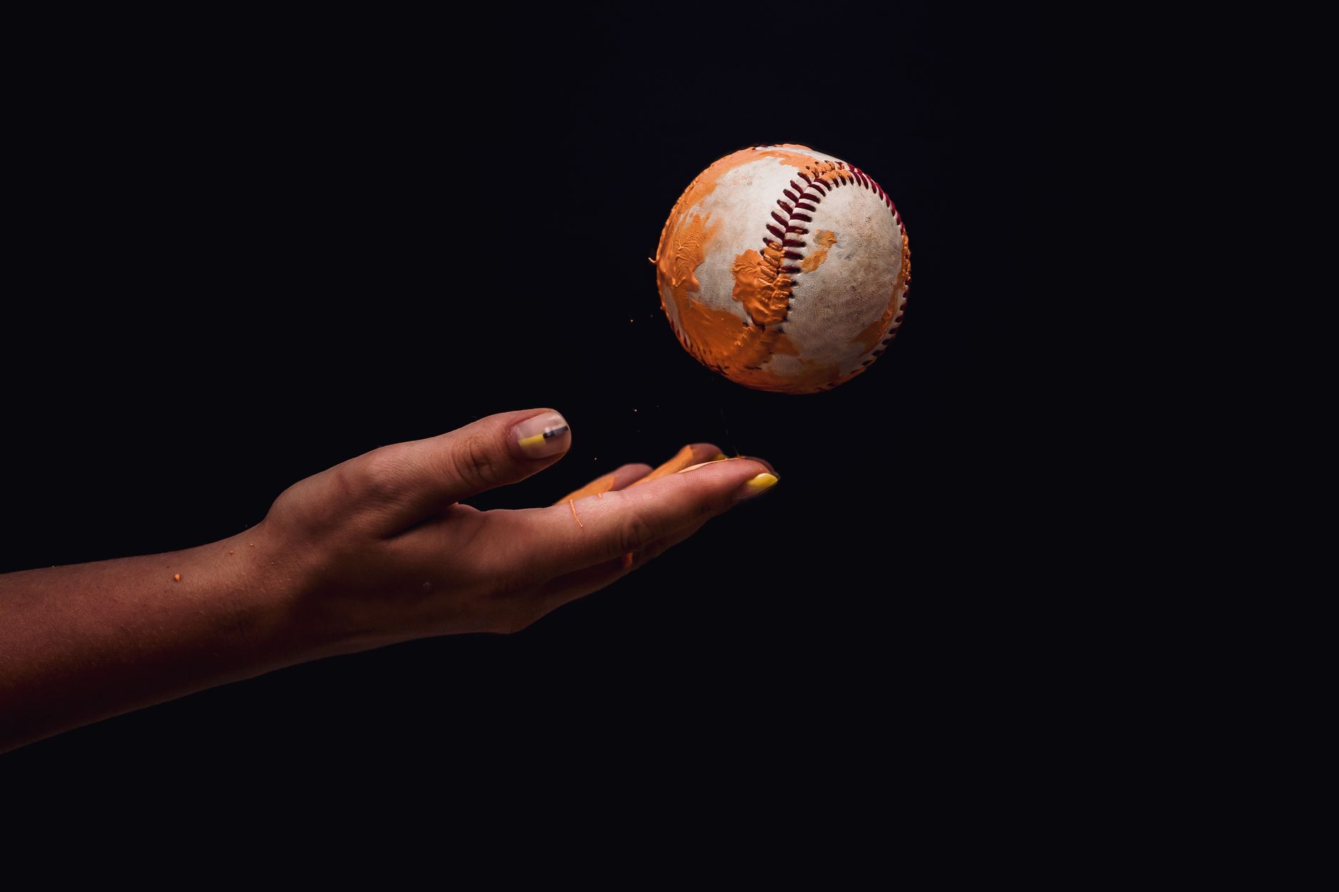 A hand tosses a paint-covered baseball, captured against a dark backdrop.