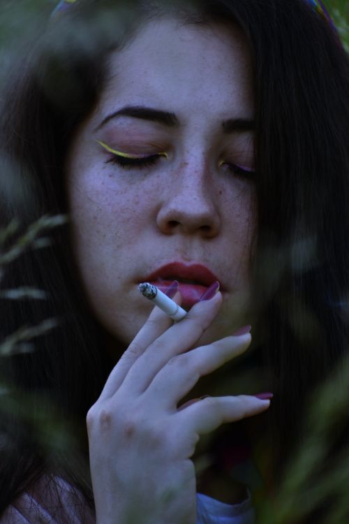 Free A captivating portrait of a woman with red lips holding a cigarette outdoors. Stock Photo
