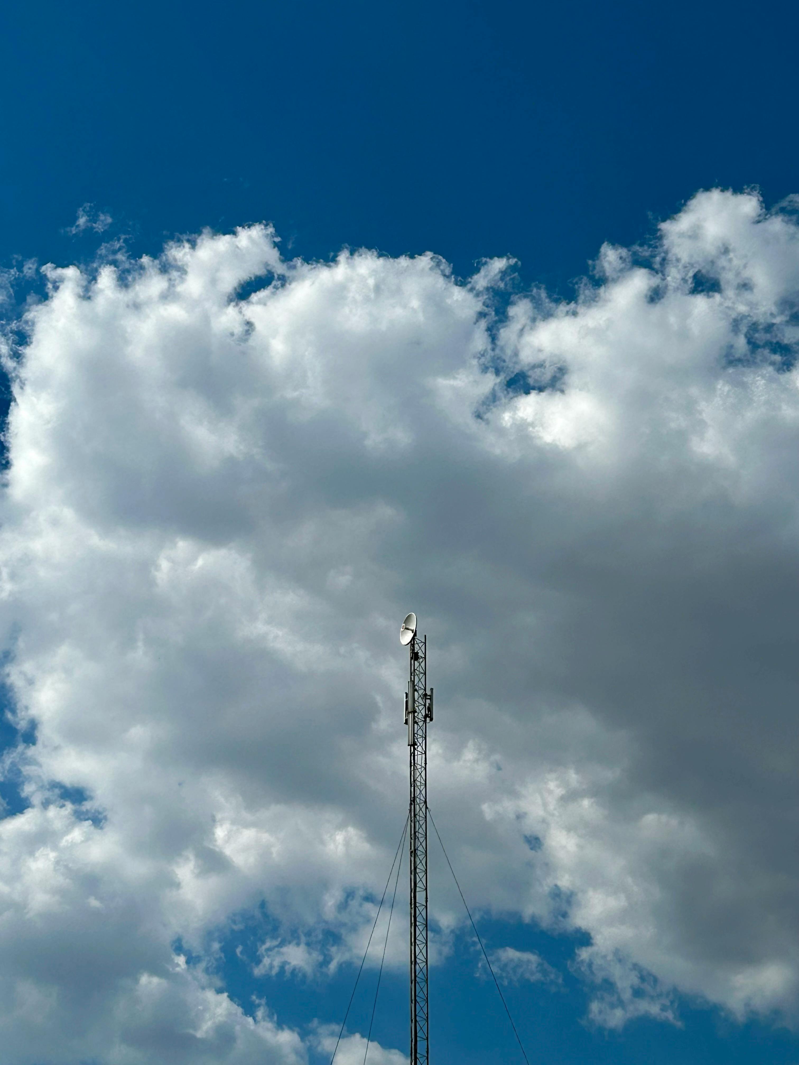 A tall transmitter tower reaching into a bright sky with scattered clouds.
