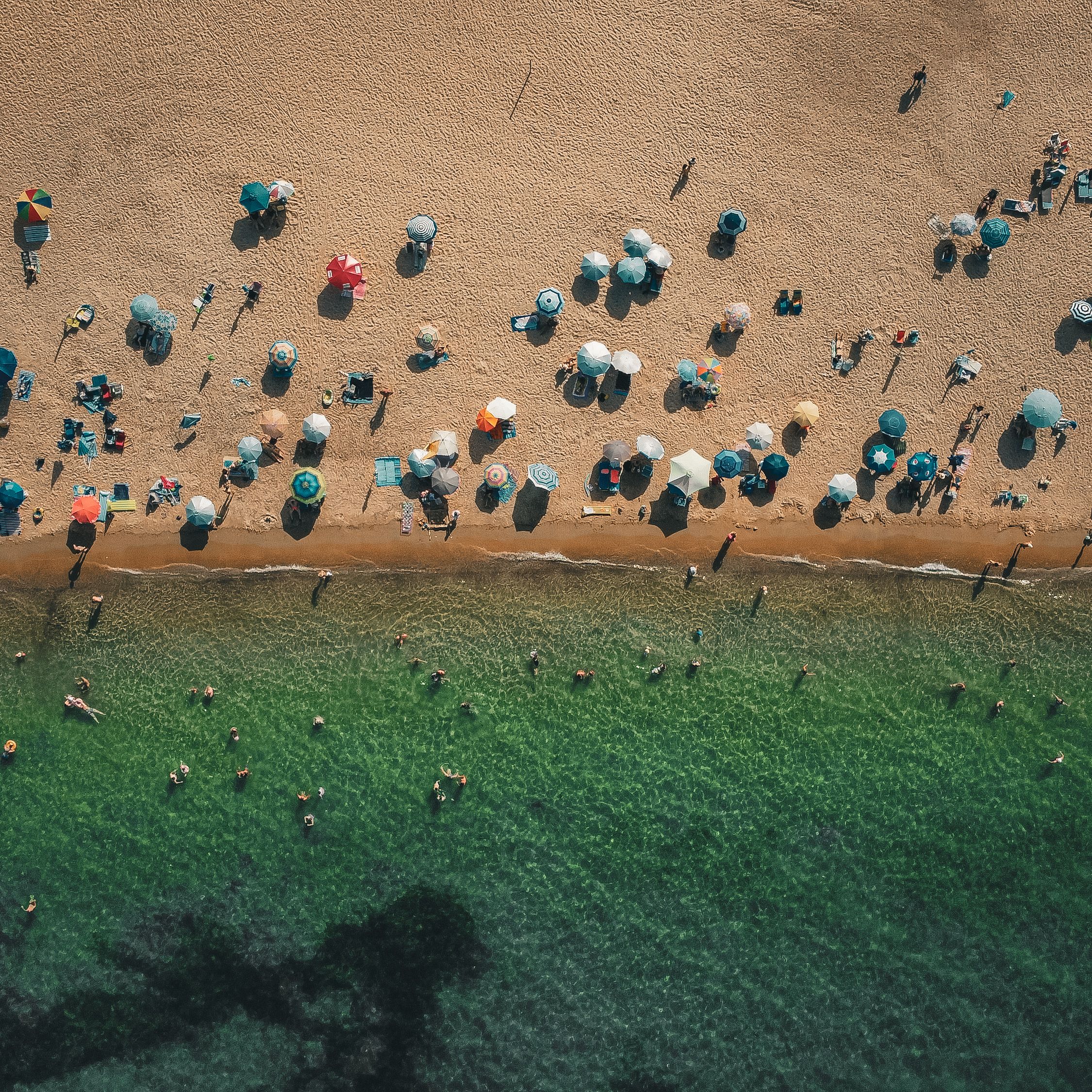 A vibrant summer beach scene from above with umbrellas and people enjoying the sun and sea.