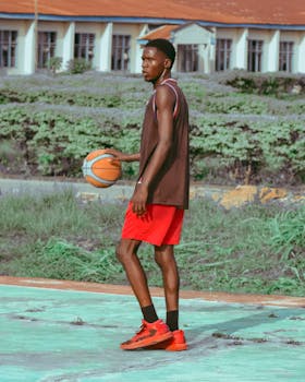 A young black man in sportswear dribbling a basketball outdoors on a sunny day.