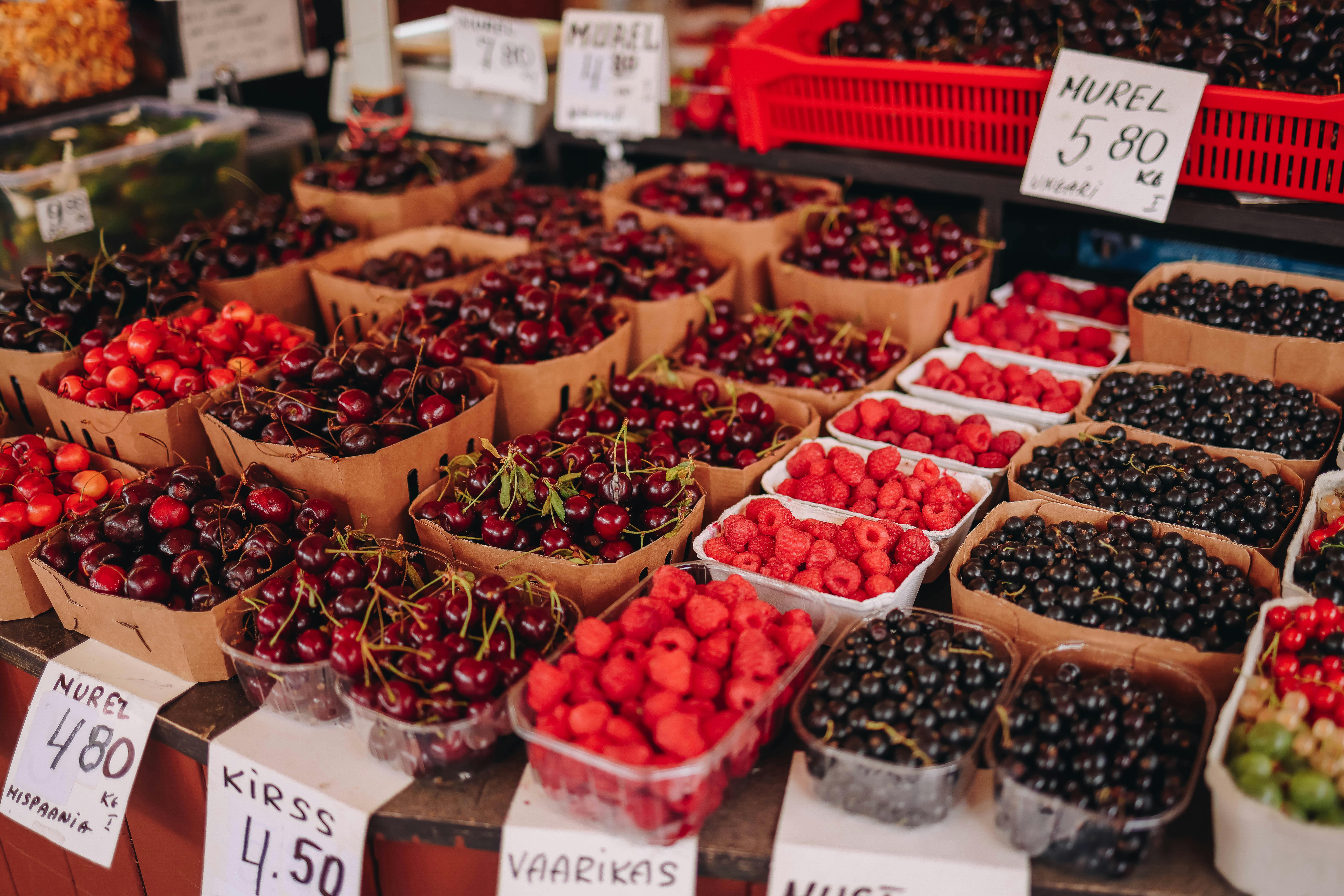 Free Vibrant market stall with fresh cherries and raspberries in paper baskets. Stock Photo