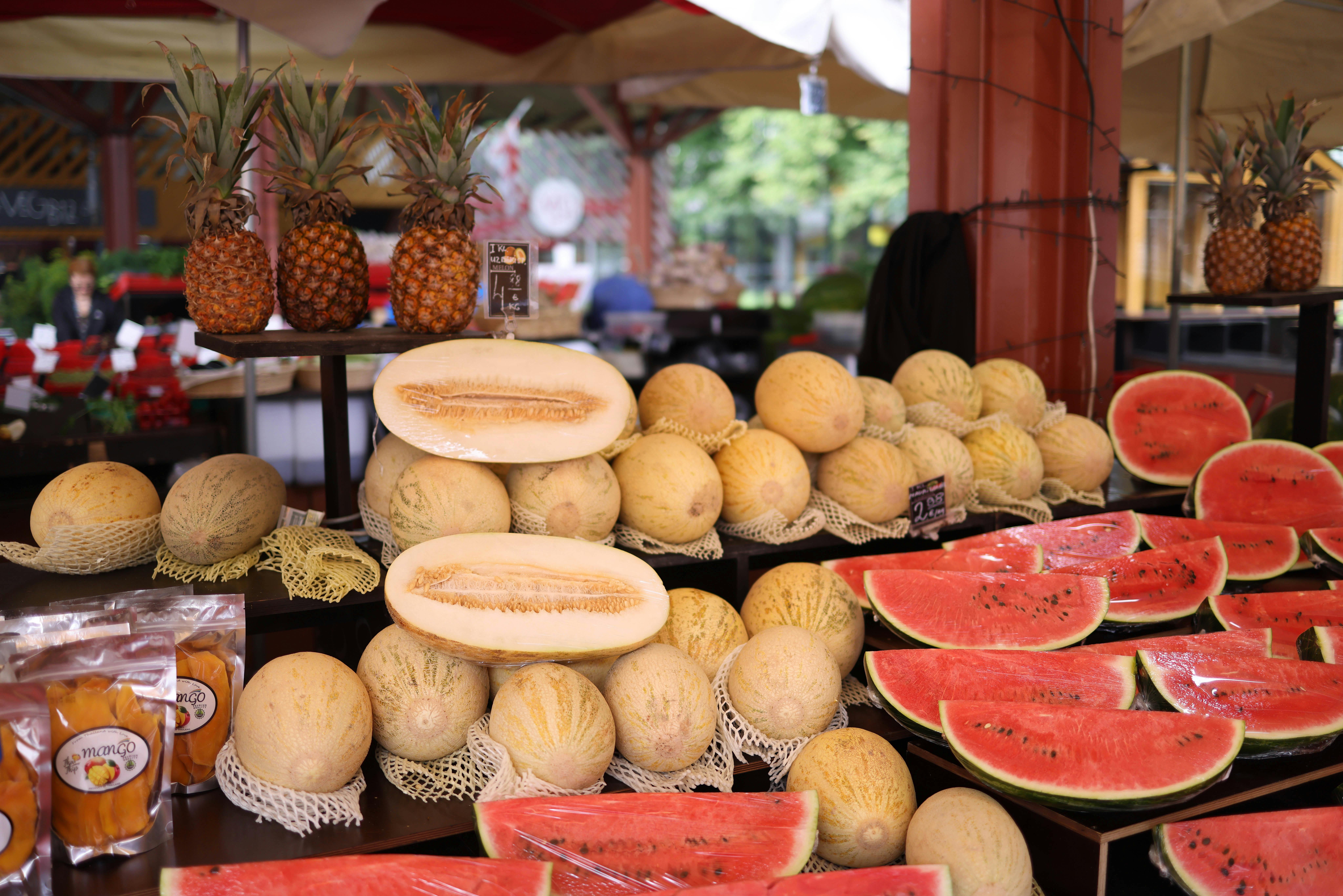 A colorful display of yellow melons, watermelons, and pineapples at a market stall showcasing fresh produce.