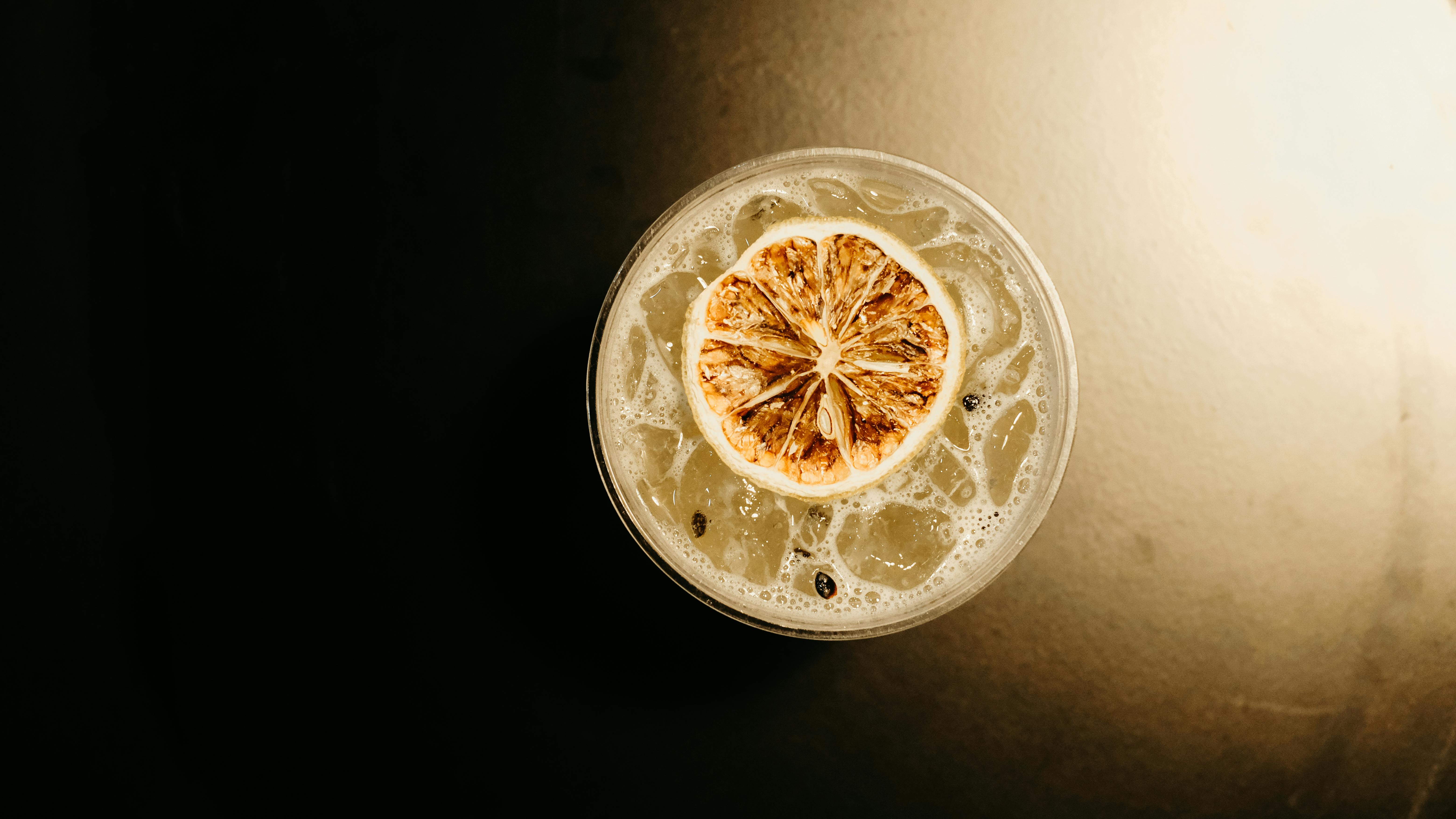 A glass of kombucha with bubbles and a slice of ginger floating