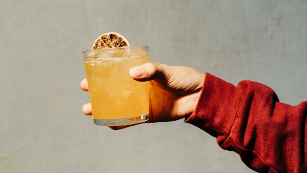 A vibrant citrus drink with ice held in a hand, showcasing a refreshing summer beverage.