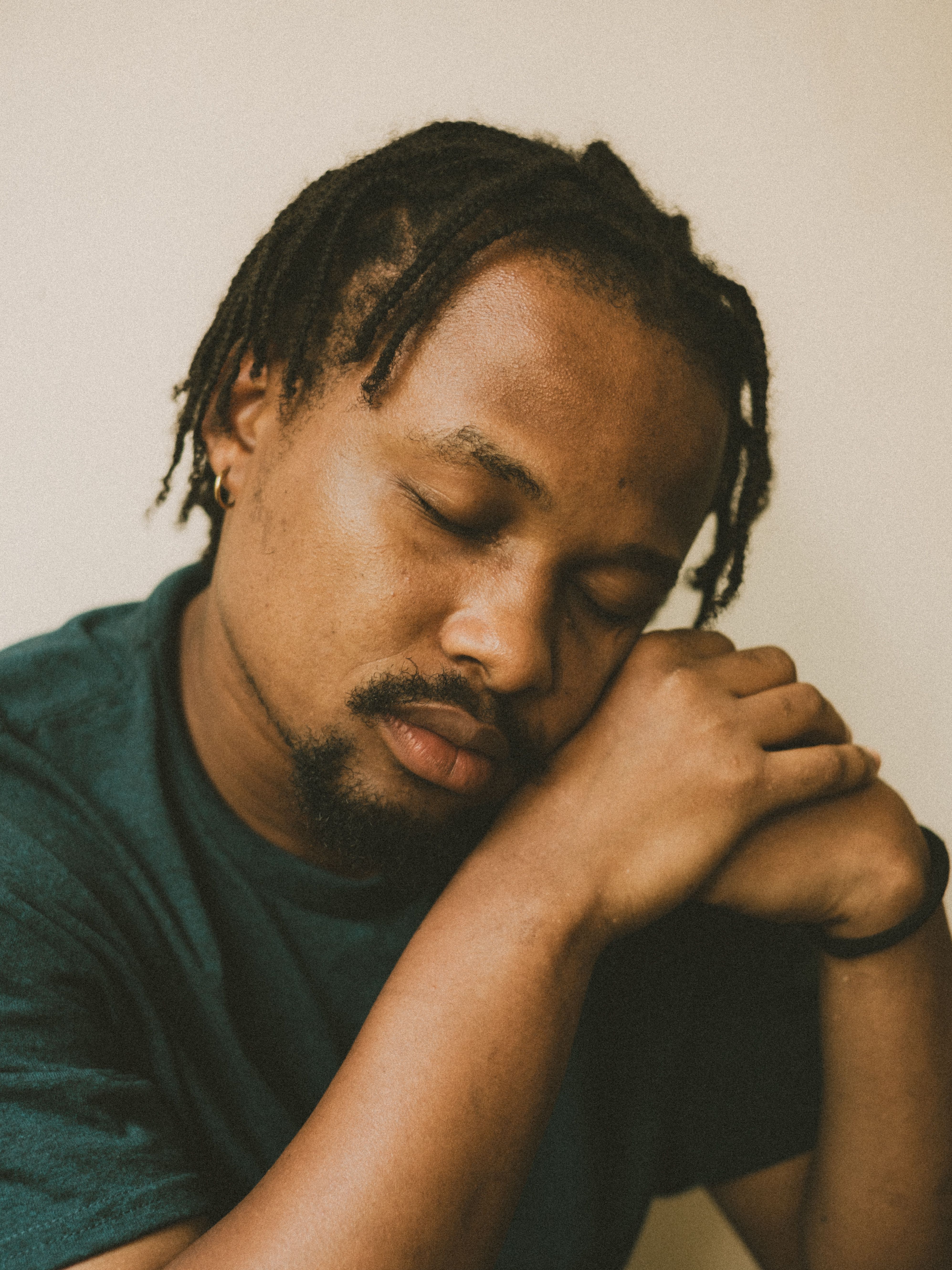 A thoughtful portrait of a man with braided hair, eyes closed, in a calm pose.