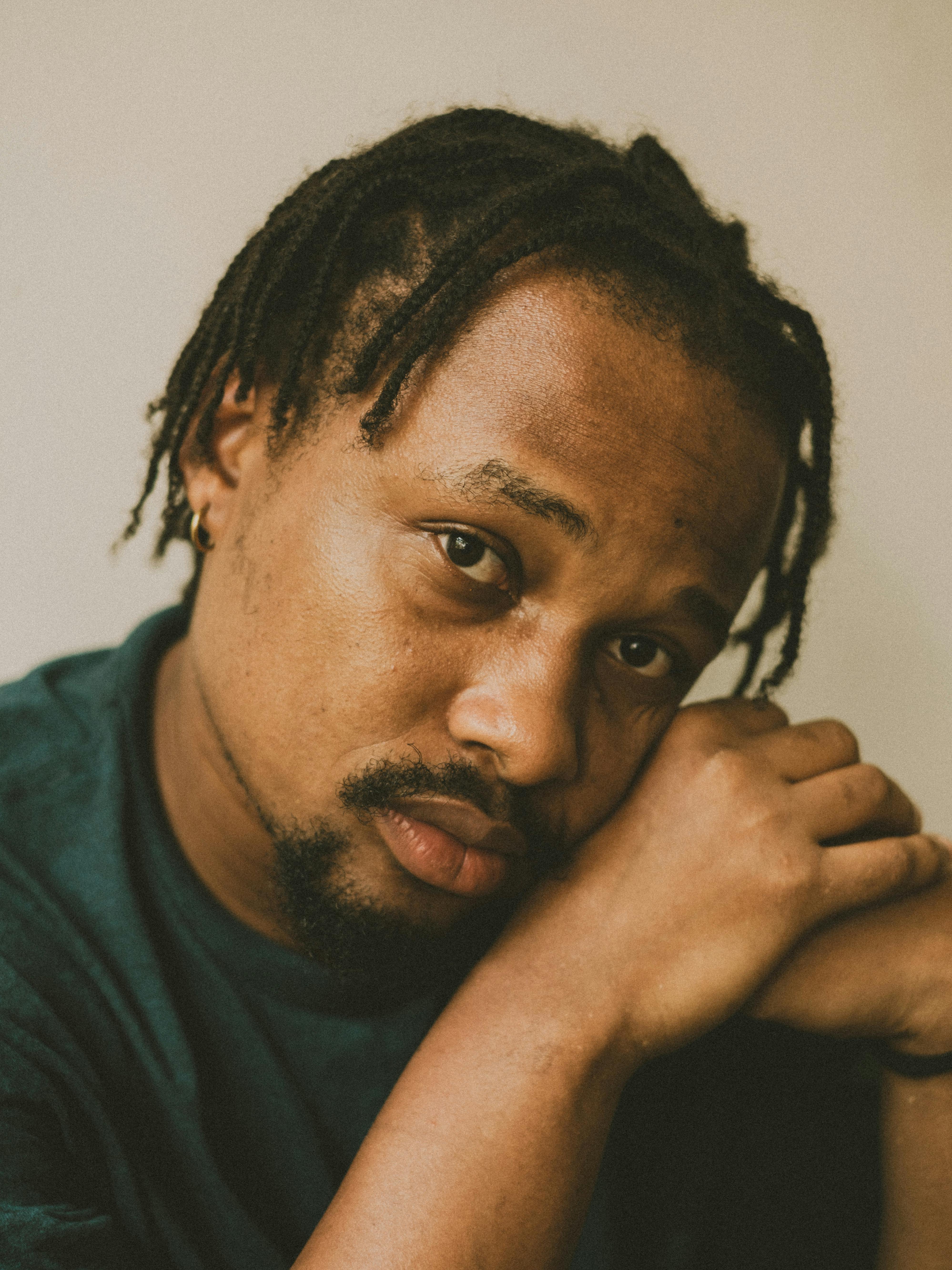 Captivating portrait of a man with braided hair resting his head on his hands, displaying a contemplative expression.
