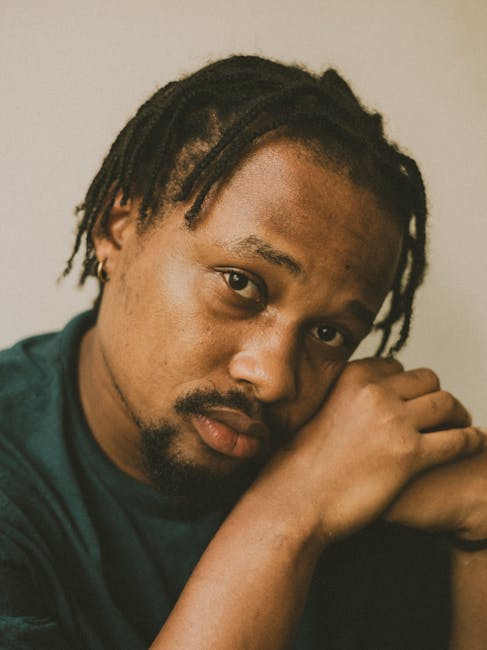 Captivating portrait of a man with braided hair resting his head on his hands, displaying a contemplative expression.