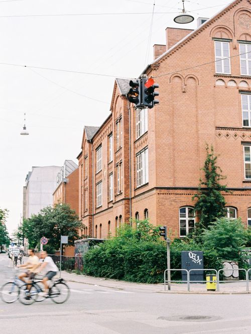 Free A city street scene featuring a historic brick building and cyclists passing by in an urban area. Stock Photo