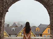 一位身穿花卉连衣裙的女子透过古老的石砌拱门，凝视着朦胧的城镇景观，营造出一幅宁静的景象