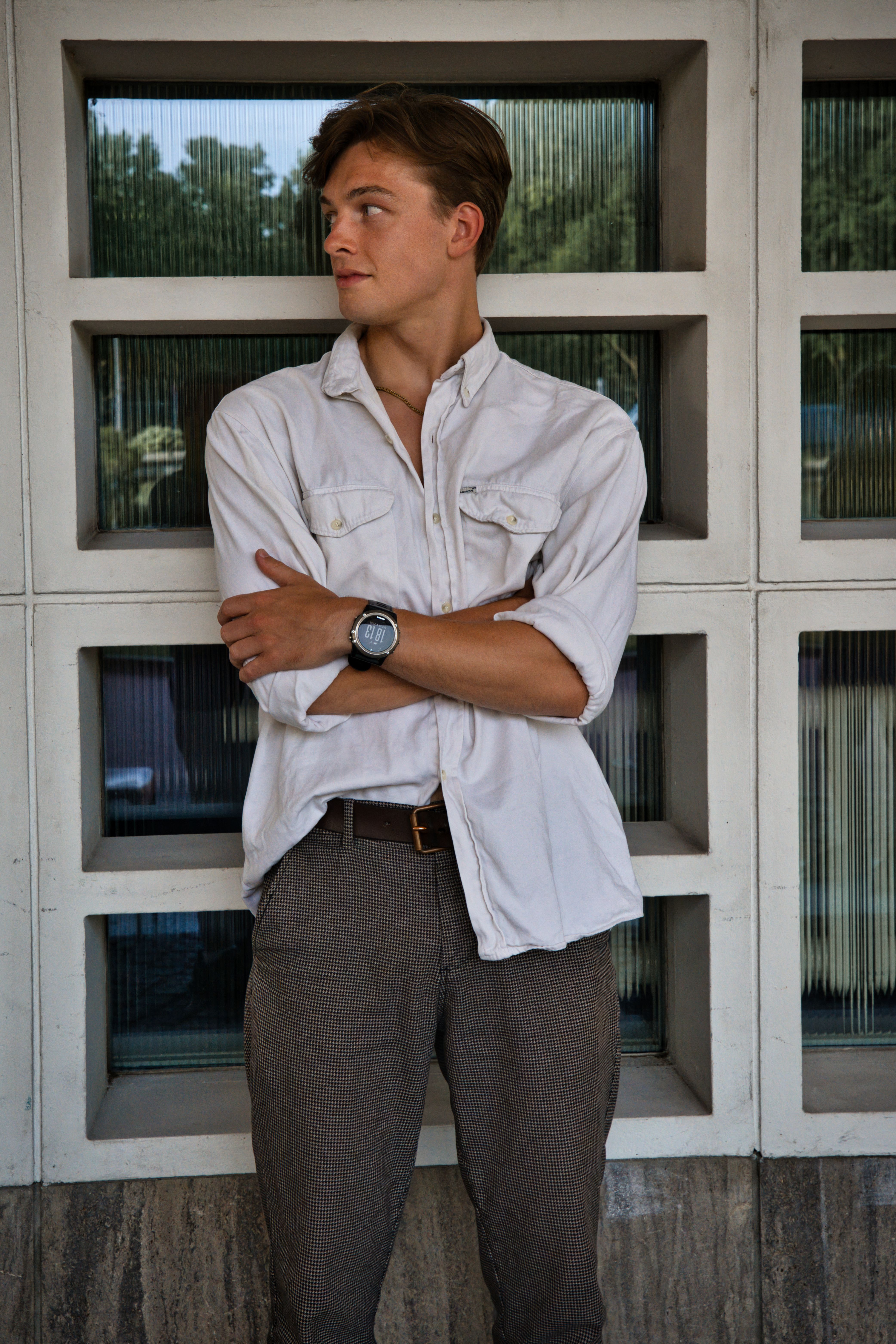 Dominant fashion portrait of a young man standing outside a Berlin building, exuding modern urban style.