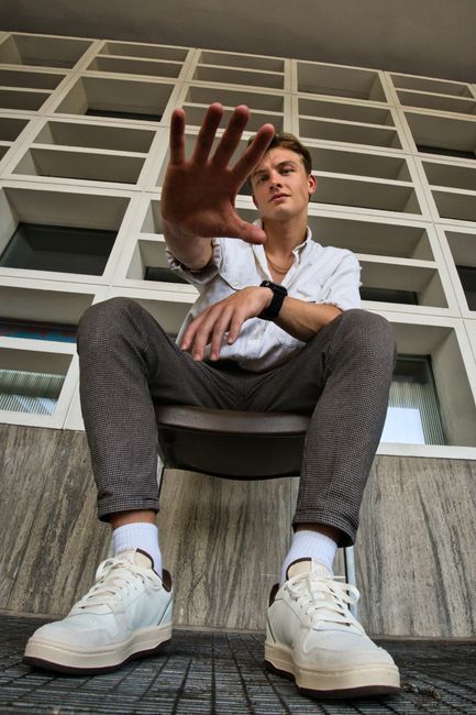 Fashionable young man sits stylishly outdoors in Berlin urban architecture.