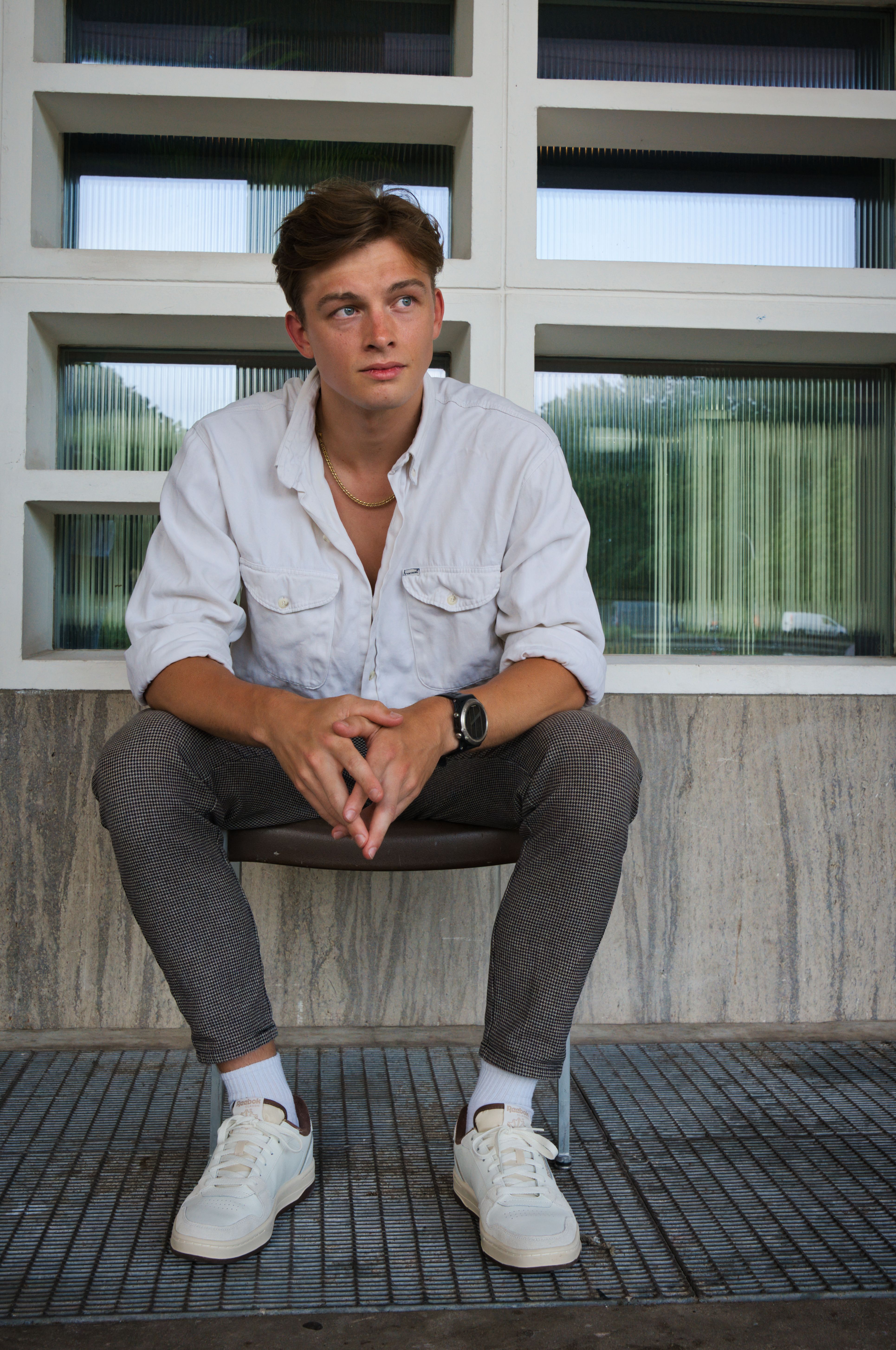 Portrait of a young man sitting stylishly in an urban environment, exuding cool and modern fashion sense.