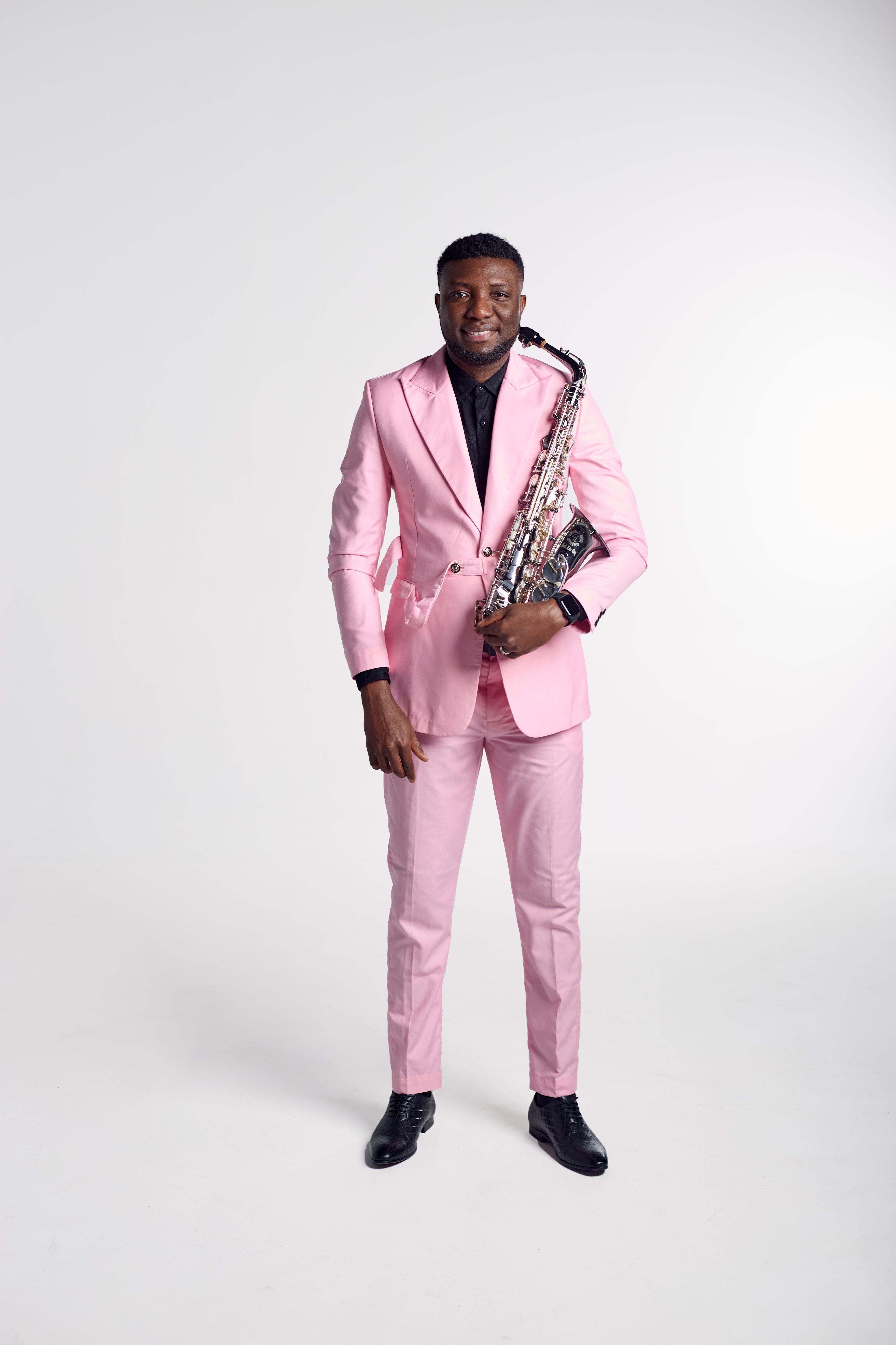 Saxophonist in a stylish pink suit posing with a saxophone in studio.