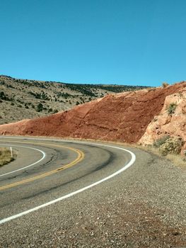 Winding road with striking red rock formations in a desert landscape under a clear blue sky.