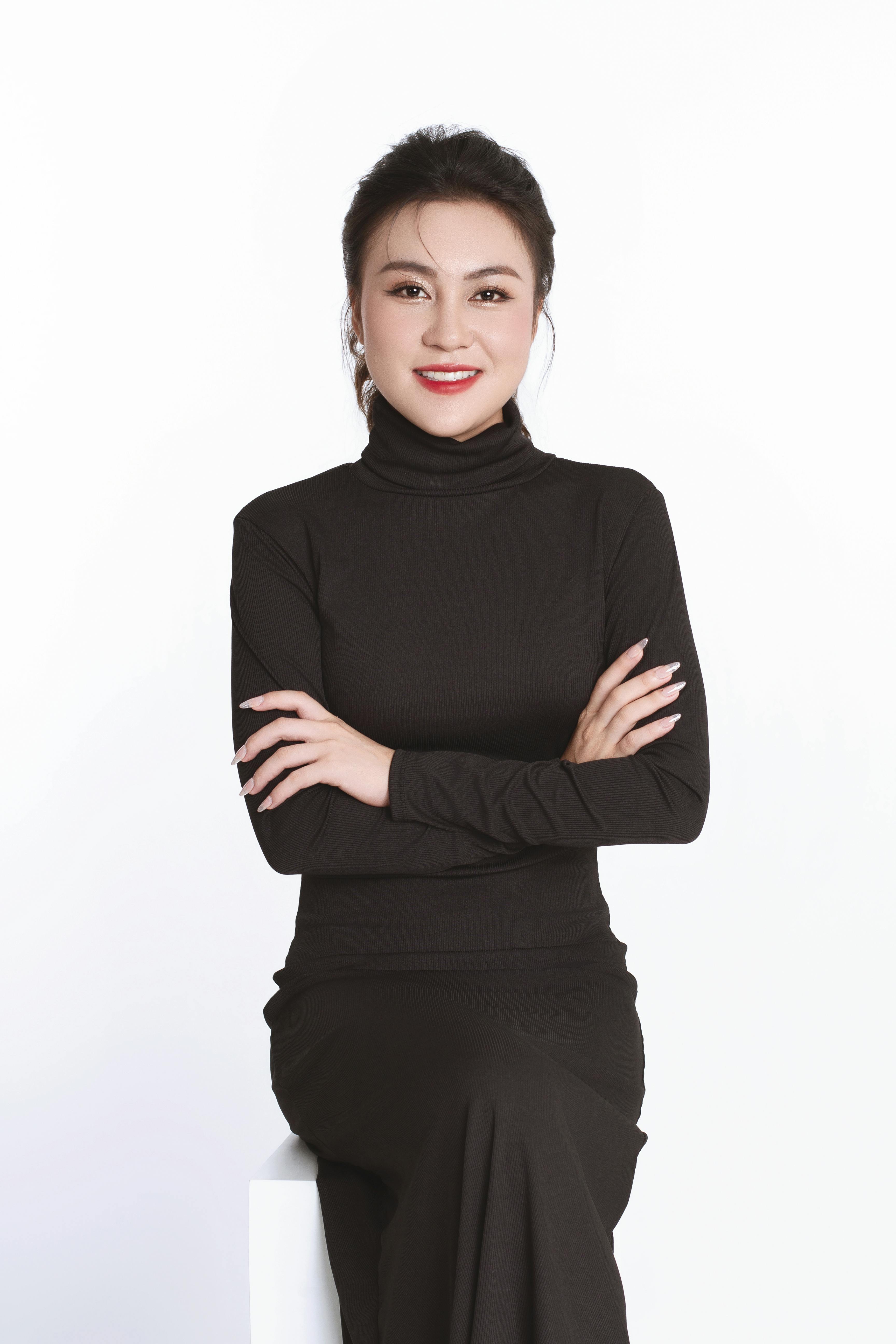 Portrait of an elegant Asian businesswoman in a black dress, posing with a confident smile in a studio.