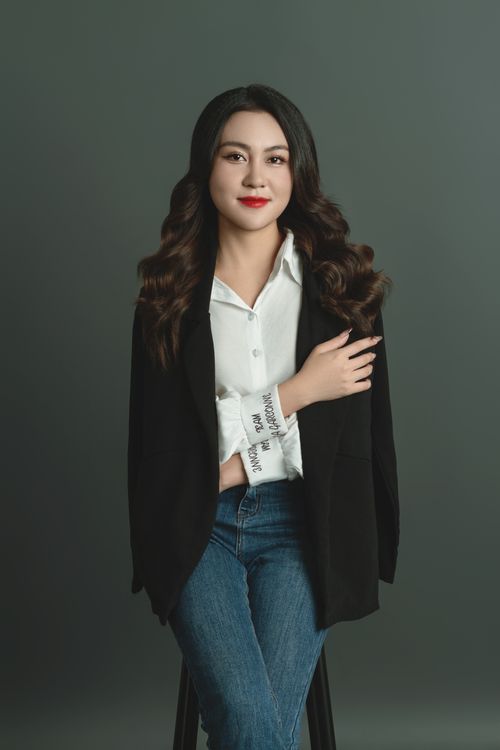 Free Confident businesswoman in a casual yet stylish outfit sitting against a simple studio backdrop. Stock Photo