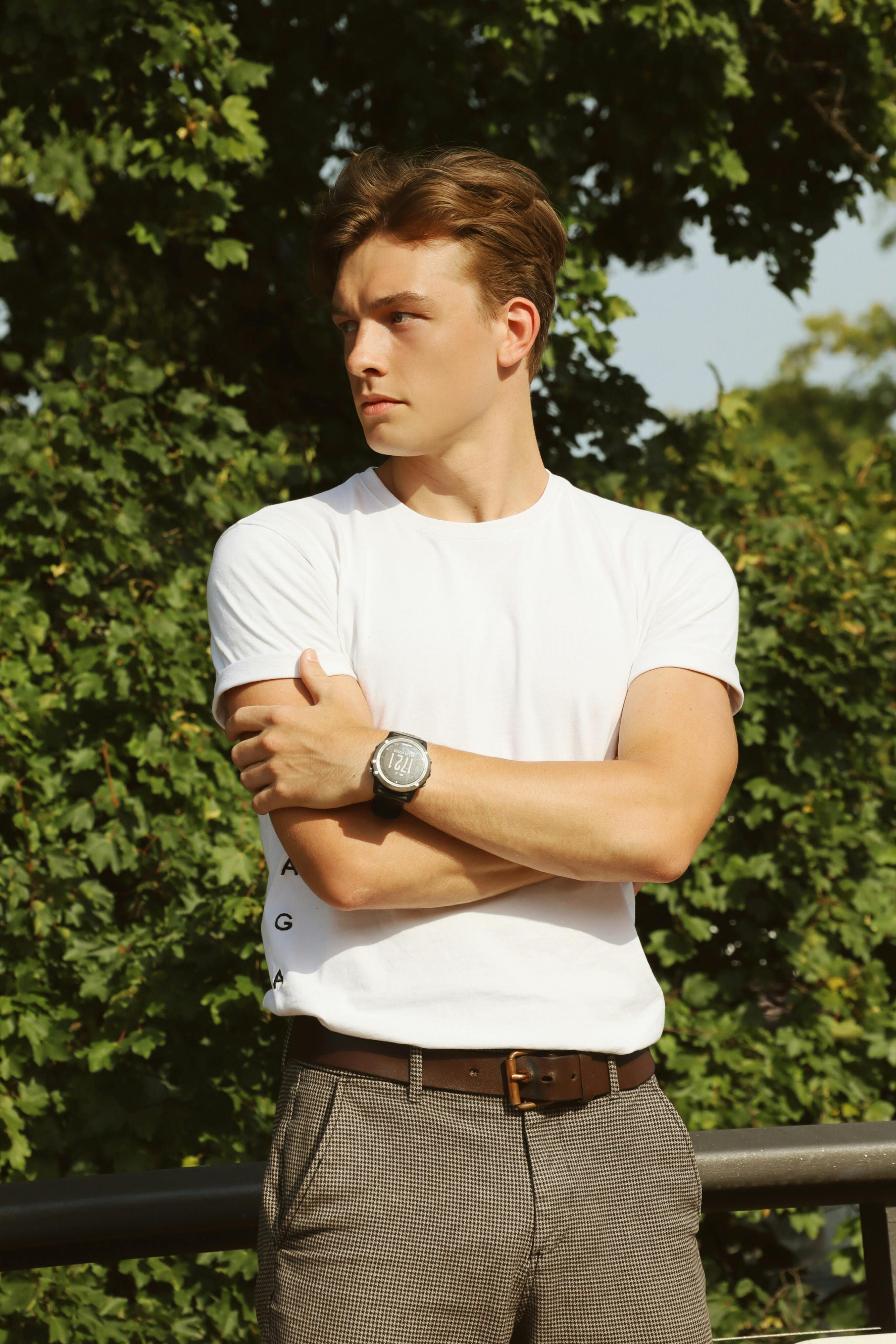 Caucasian man in a white t-shirt poses confidently in a Berlin park during the day.
