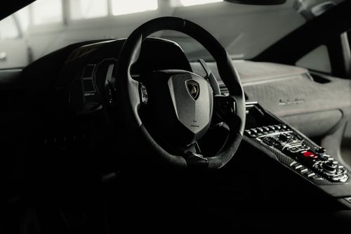 Free Close-up of Lamborghini interior showcasing steering wheel and dashboard in dim lighting. Stock Photo