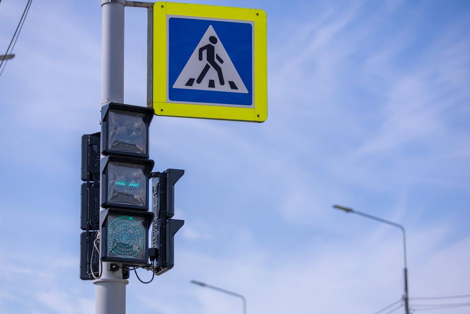 Traffic lights with pedestrian sign at a street intersection under a clear blue sky.