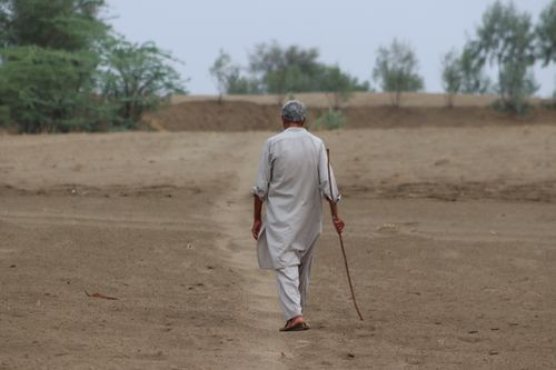 Free Elderly man with a cane walking alone through a vast desert landscape. Stock Photo