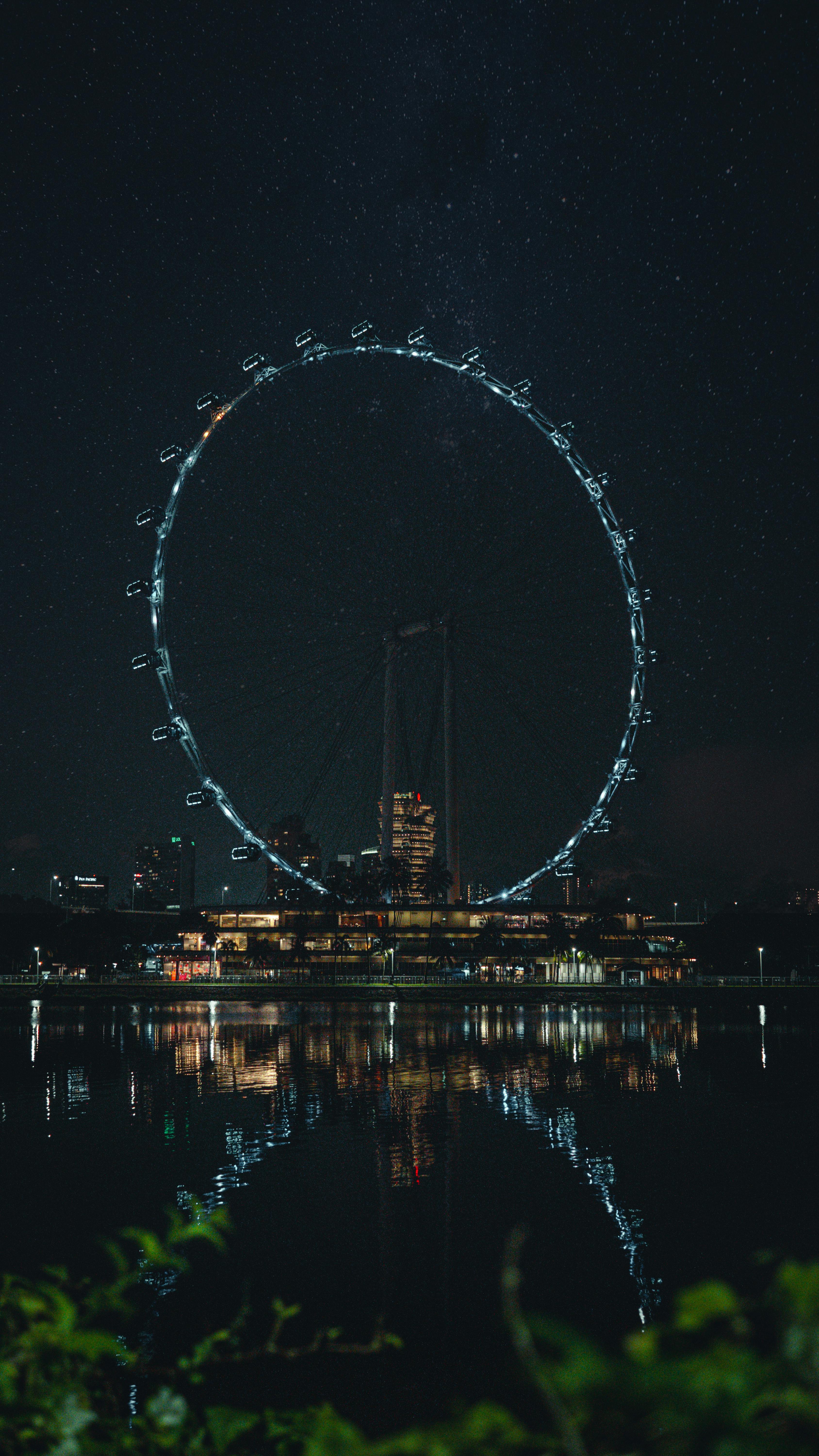 Stunning nighttime image of a Ferris wheel reflecting on a serene water surface.